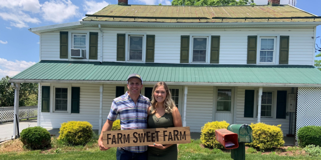 Couple standing in front of white farmhouse with green shutters