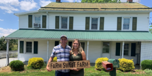 Couple standing in front of white farmhouse with green shutters