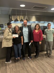 five individuals in a kitchen one being presented a check