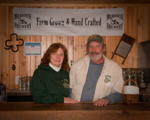 woman and man in front of a wooden wall at their brewery