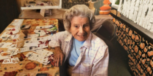 a women at a table with paper cutouts smiling at the camera.