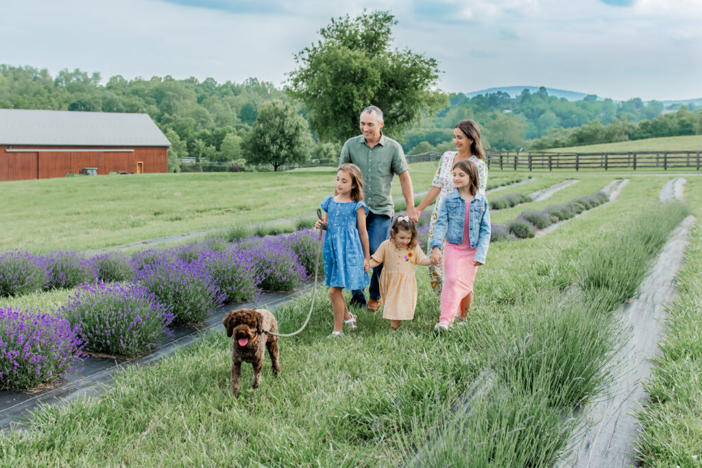 a family of 5, a man, women, and three young kids with a brown dog in a lavender felid