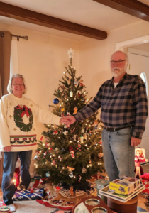 A man and his wife standing in front of a Christmas tree holding hands.