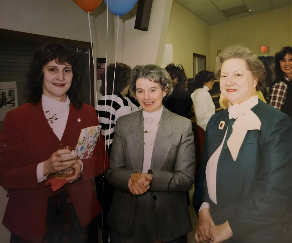 three women standing next to eachother with balloons in the background. 