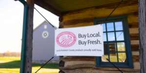 a sign in front of a log cabin that says buy local. Buy fresh.