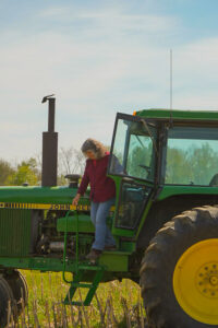 A women climbing out of the cab of a John Deer tractor